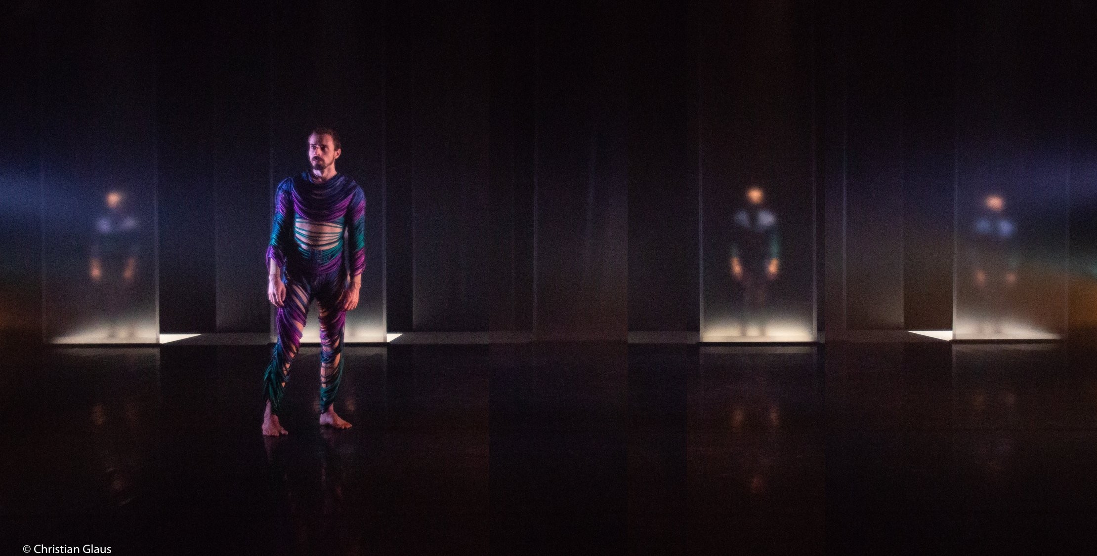 Dominik Wagner performing on stage in colorful movement costume, dimly lit